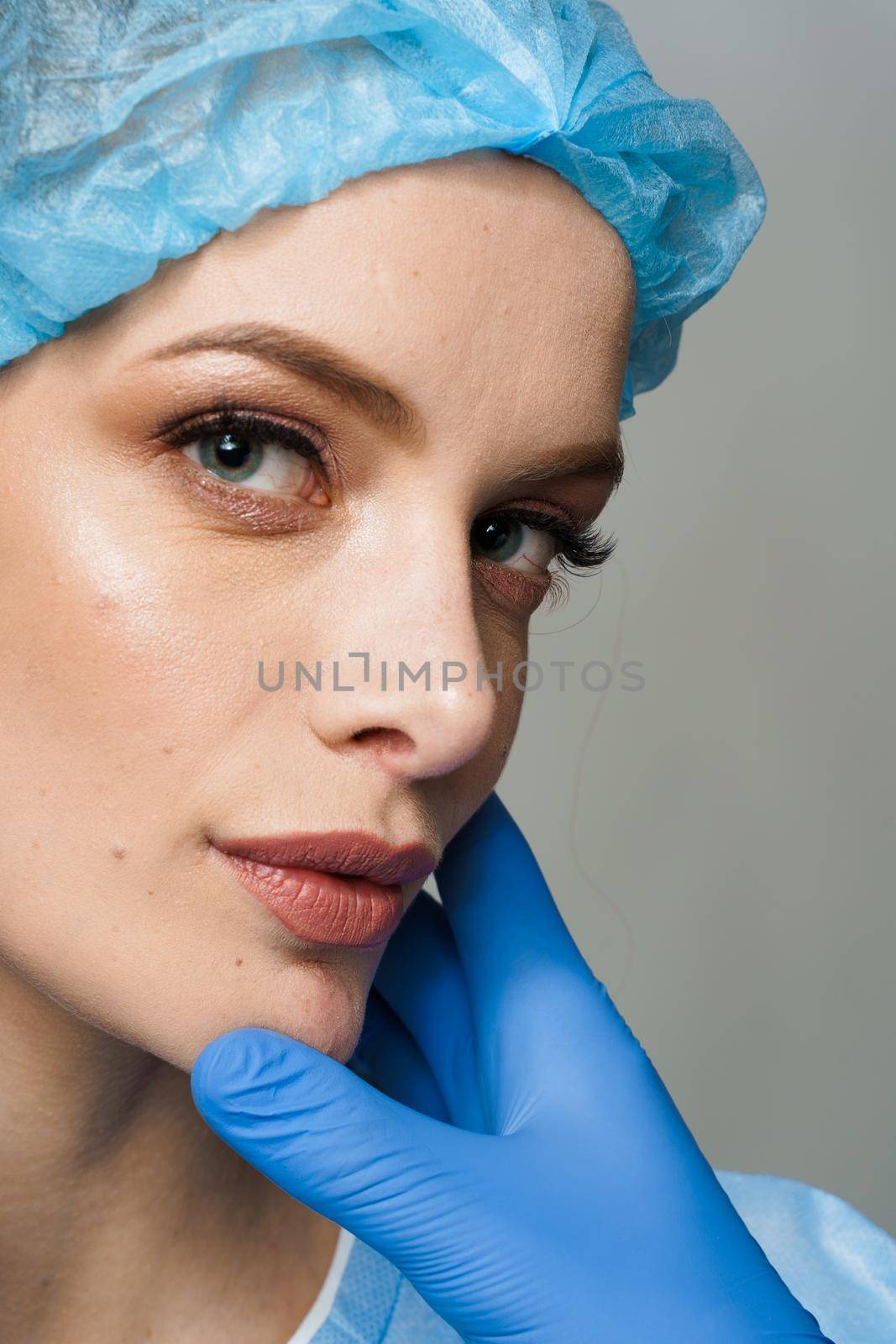 Consultation with plastic surgeon on white background. Cosmetic rejuvenating facial treatment. Doctor man with blue medical gloves touches girl face.