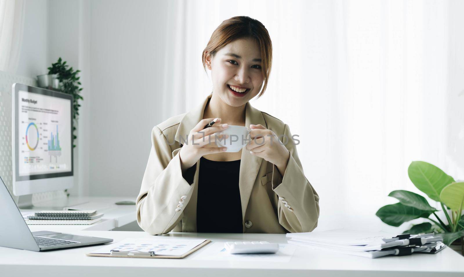 Smiling Asian businesswoman holding a coffee mug and laptop at the office. Looking at the camera. by wichayada