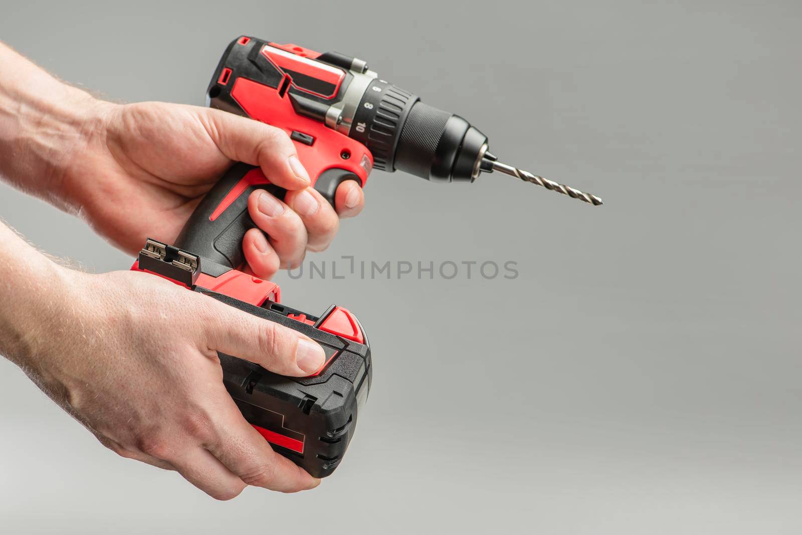 a man's hand removes the battery from a cordless tool. A man inserts a battery into a screwdriver. Repair and construction concept on gray background.