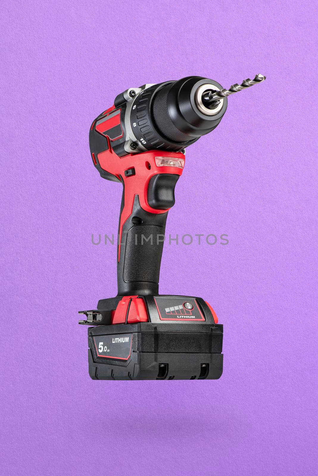 Cordless drill in black and red. Screwdriver with a drill on a purple background. Modern carpentry cordless tool close-up. by SERSOL