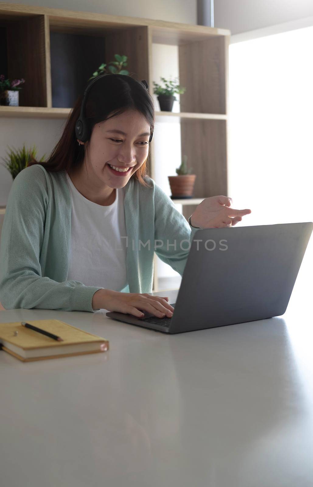 Asian student in casual clothes explaining homework on video conference with teachers on laptop computers at home by wichayada