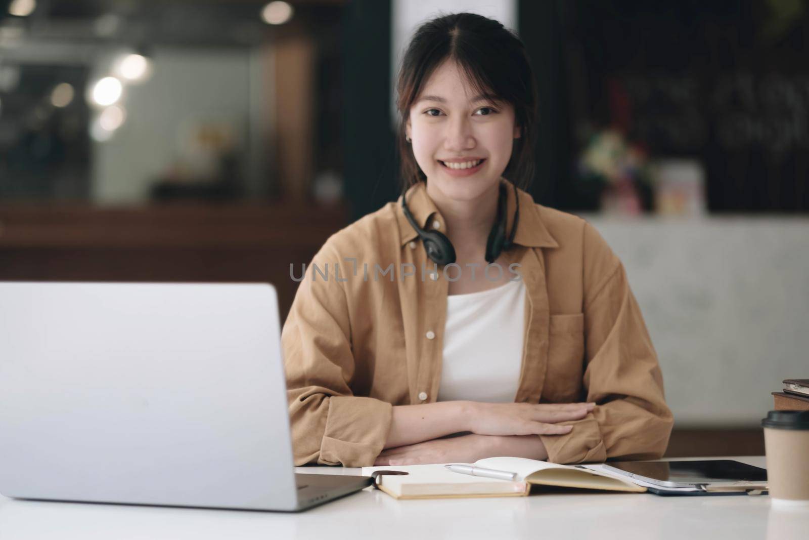 Happy young Asian student woman wearing headphones looking at webcam, looking at camera, during virtual meeting or video call talk..
