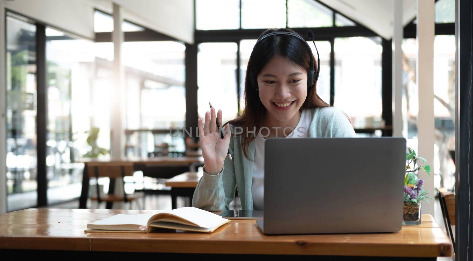 Happy young woman in headphones speaking looking at laptop making notes, girl student talking by video conference call, female teacher trainer tutoring by webcam, online training, e-coaching concept by wichayada