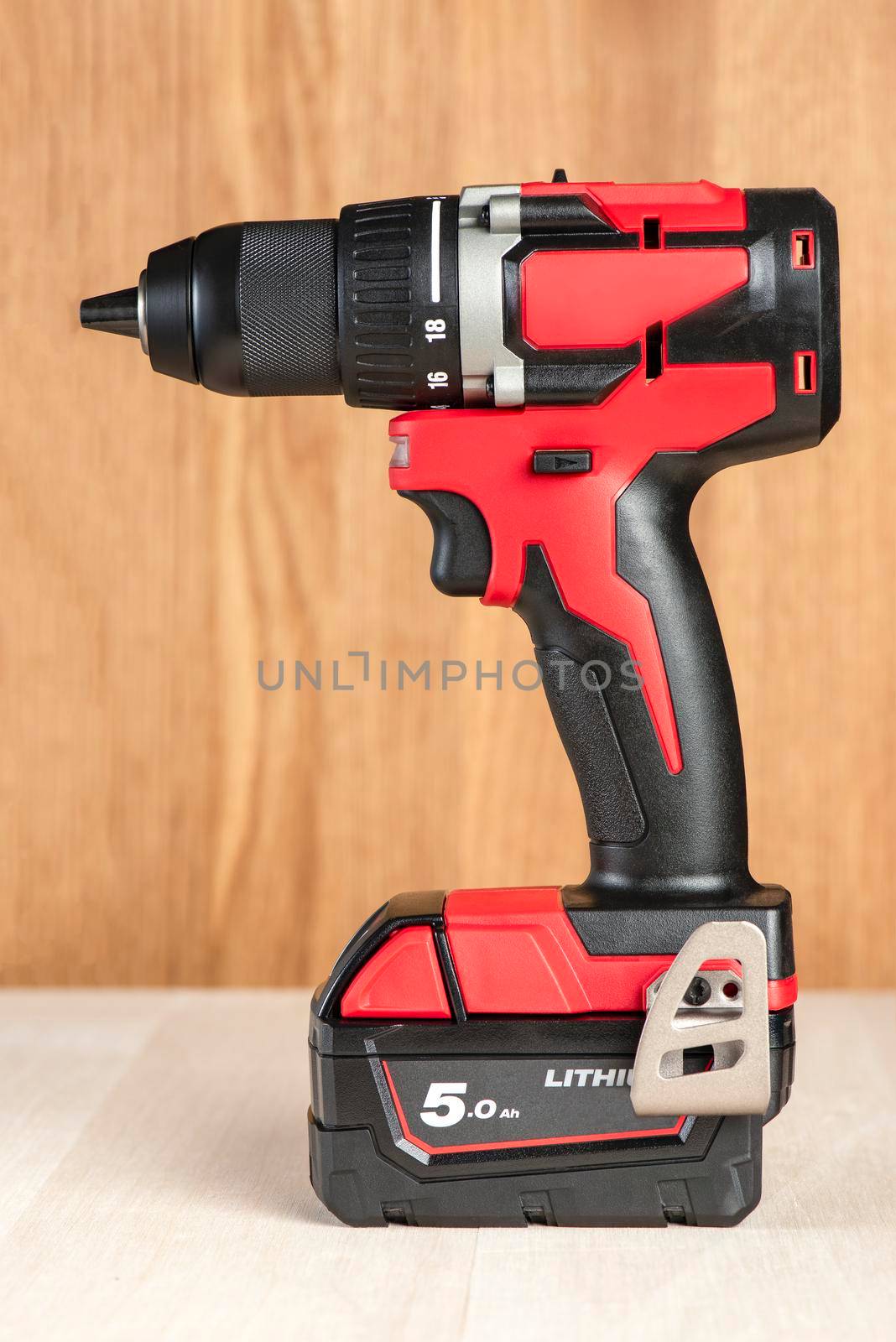 Cordless drill in black and red. A screwdriver with a drill lies on a wooden background. Modern carpentry tool close-up