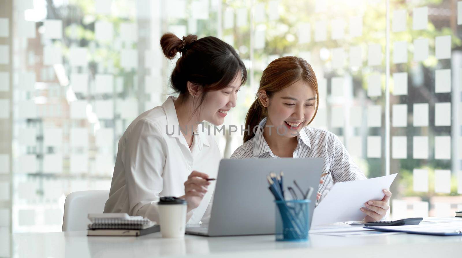Two young Asian businesswoman discuss investment project working and planning strategy. Business people talking together with laptop computer at office. by wichayada
