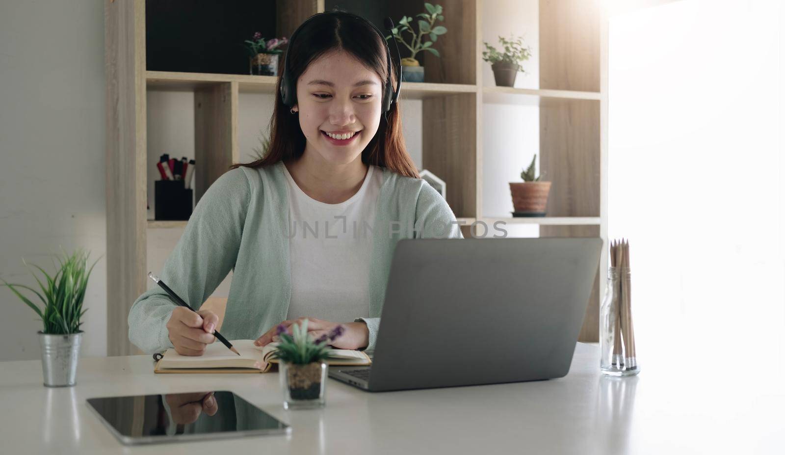 Asian schoolgirl in casual clothes is reading and doing homework video conference e-learning with teacher on laptop computer at home