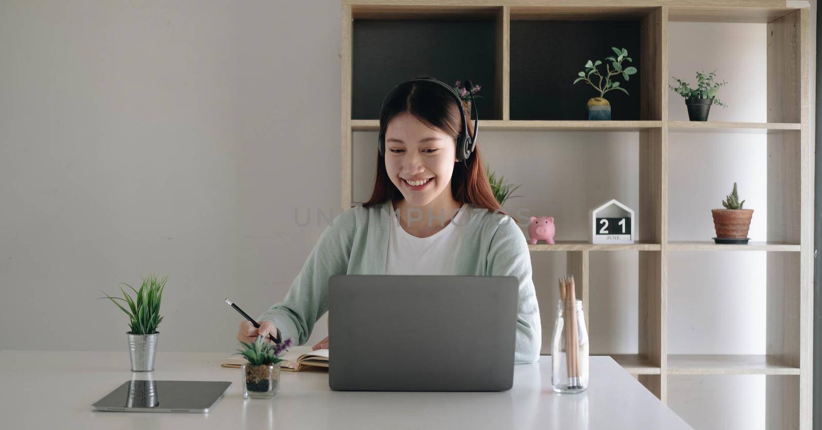 Asian schoolgirl in casual clothes is reading and doing homework video conference e-learning with teacher on laptop computer at home