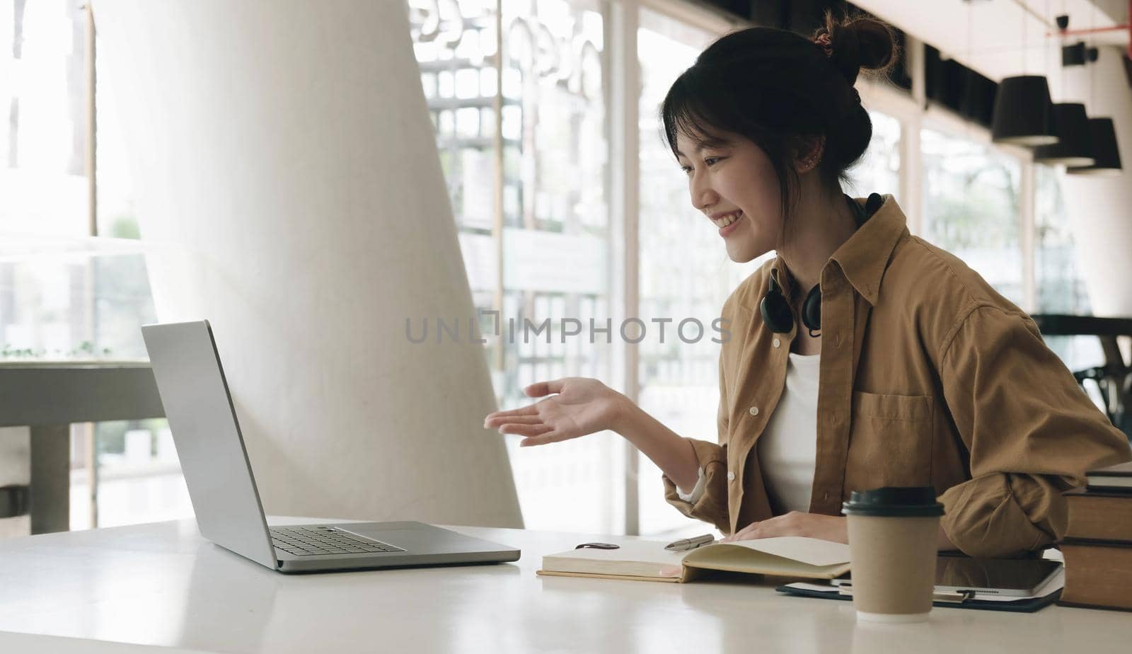 Freelance business women casual wear using laptop working call video conference with customer in workplace in living room at home. Happy young Asian girl relax sitting on desk do job in internet. by wichayada