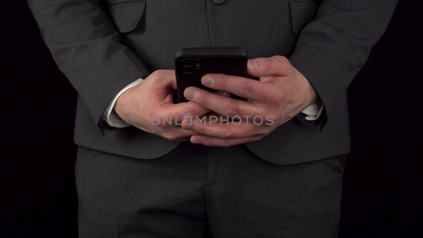 A young businessman in a suit takes out a phone from his pocket and texts in it. The waist of a man close-up on a black background. 4k