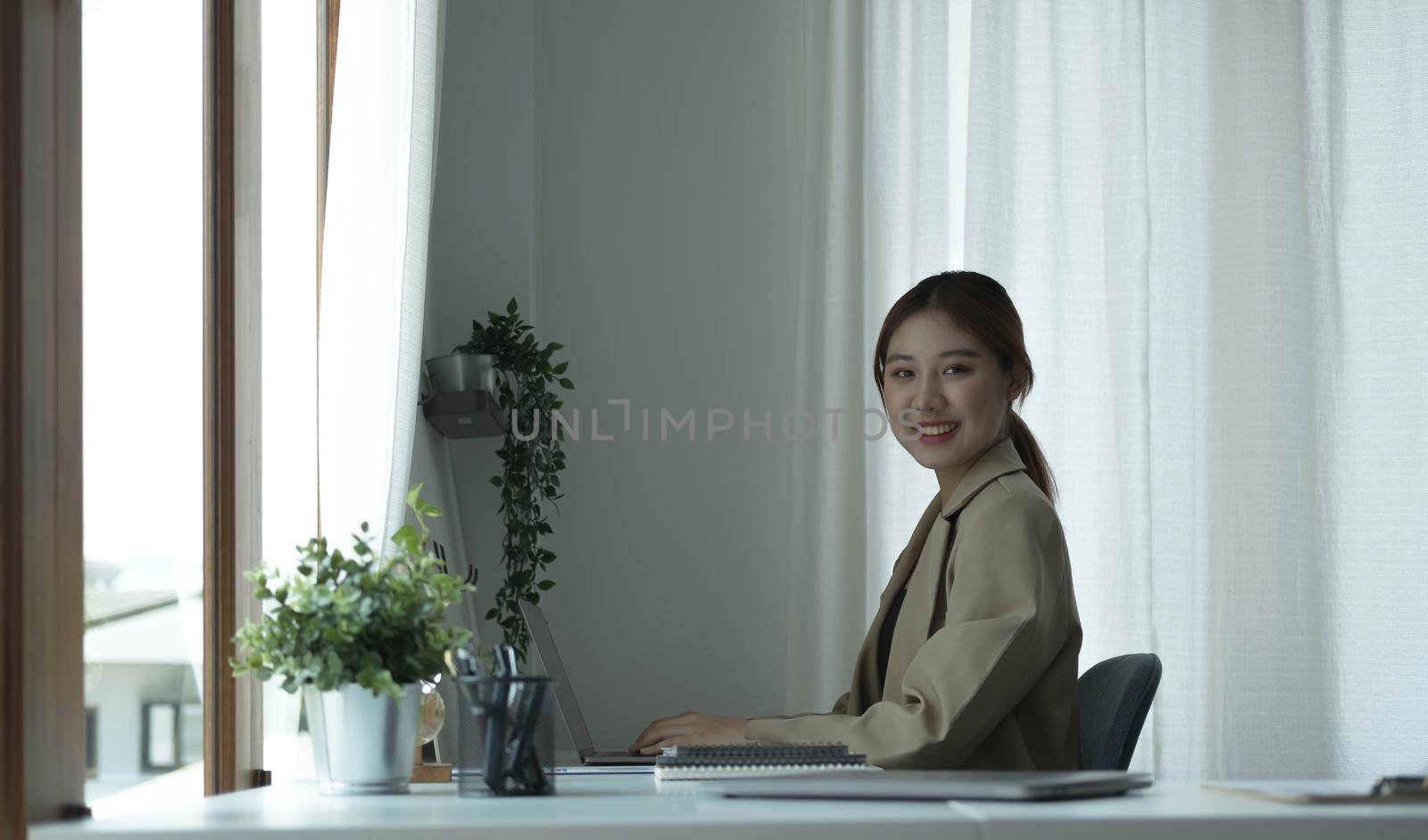 Portrait of confident young entrepreneur sitting at modern workplace and smiling to camera. by wichayada