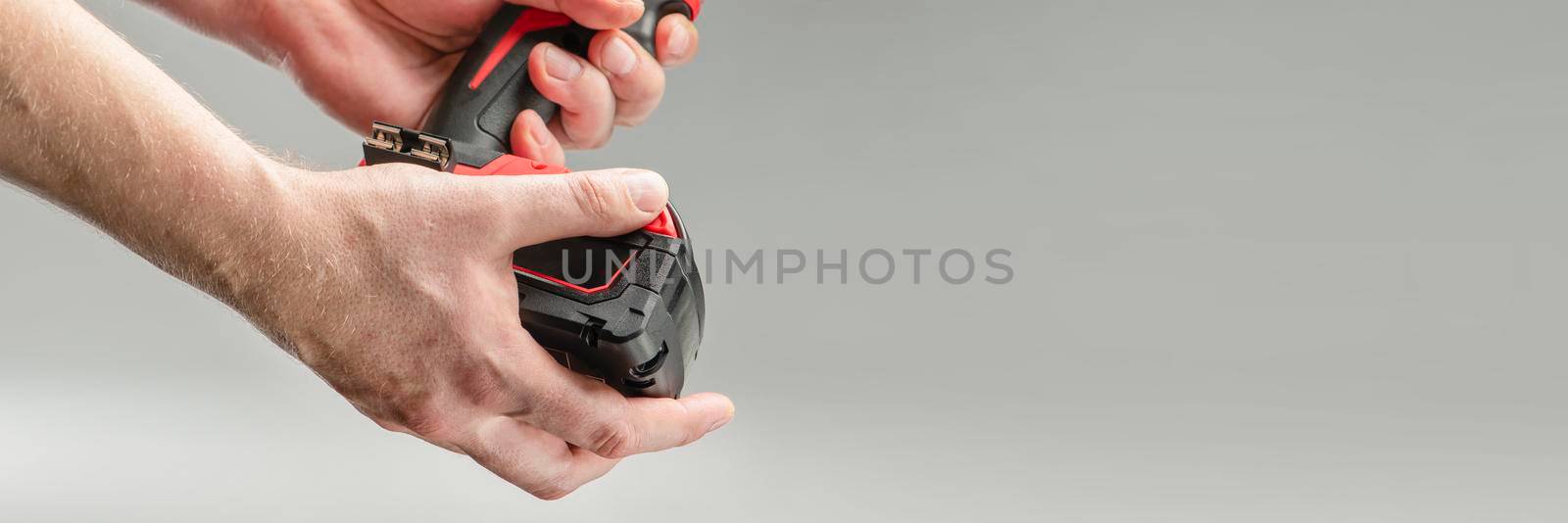 a man's hand removes the battery from a cordless tool. A man inserts a battery into a screwdriver. Repair and construction concept on gray background.