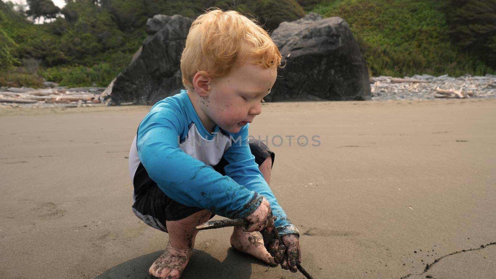 Red head child at creative play on sandy sunny beach in light blue shirt. High quality photo