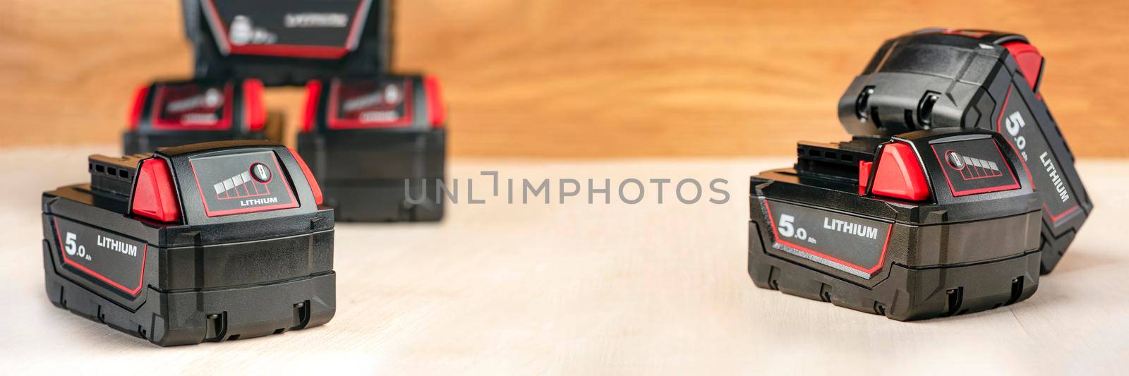 Six batteries for a screwdriver lie on a wooden background. Batteries for cordless tools with charge indicator.