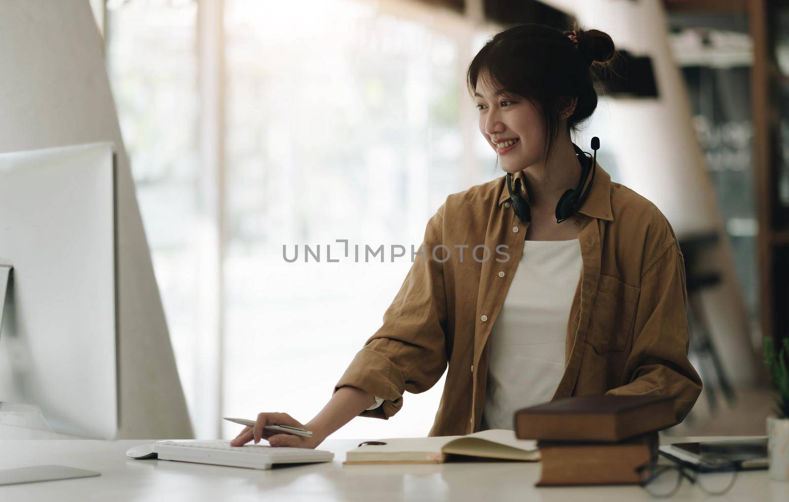 Young Asian woman wearing headphones is using a laptop at home. by wichayada