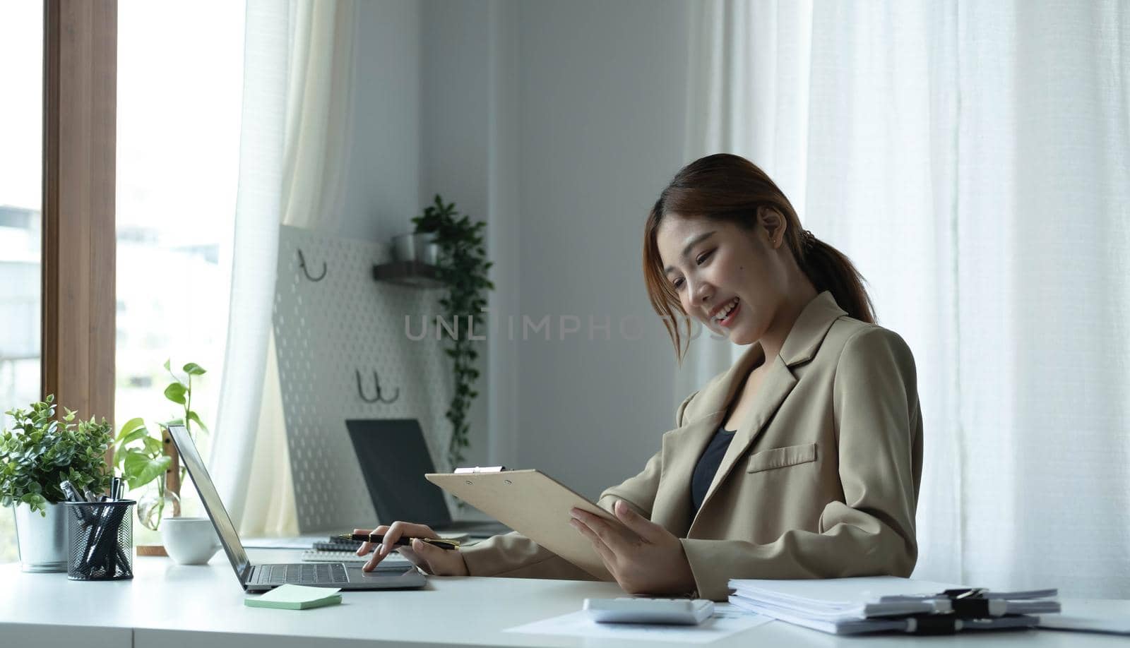 Attractive young woman sitting and her workplace and checking information on clipboard..