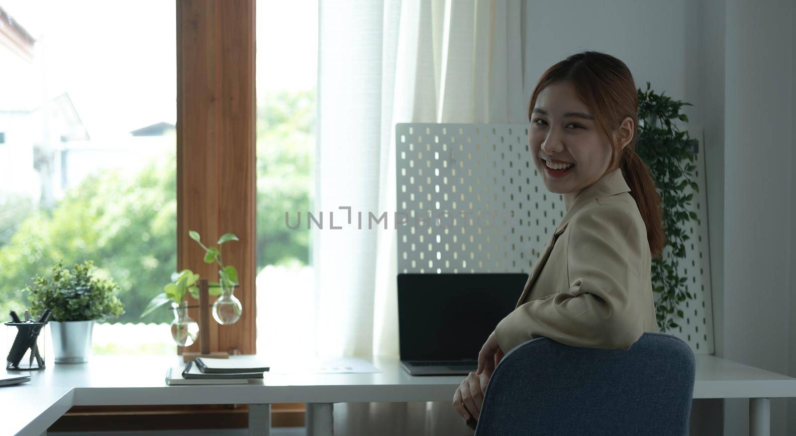 Portrait of confident young entrepreneur sitting at modern workplace and smiling to camera..