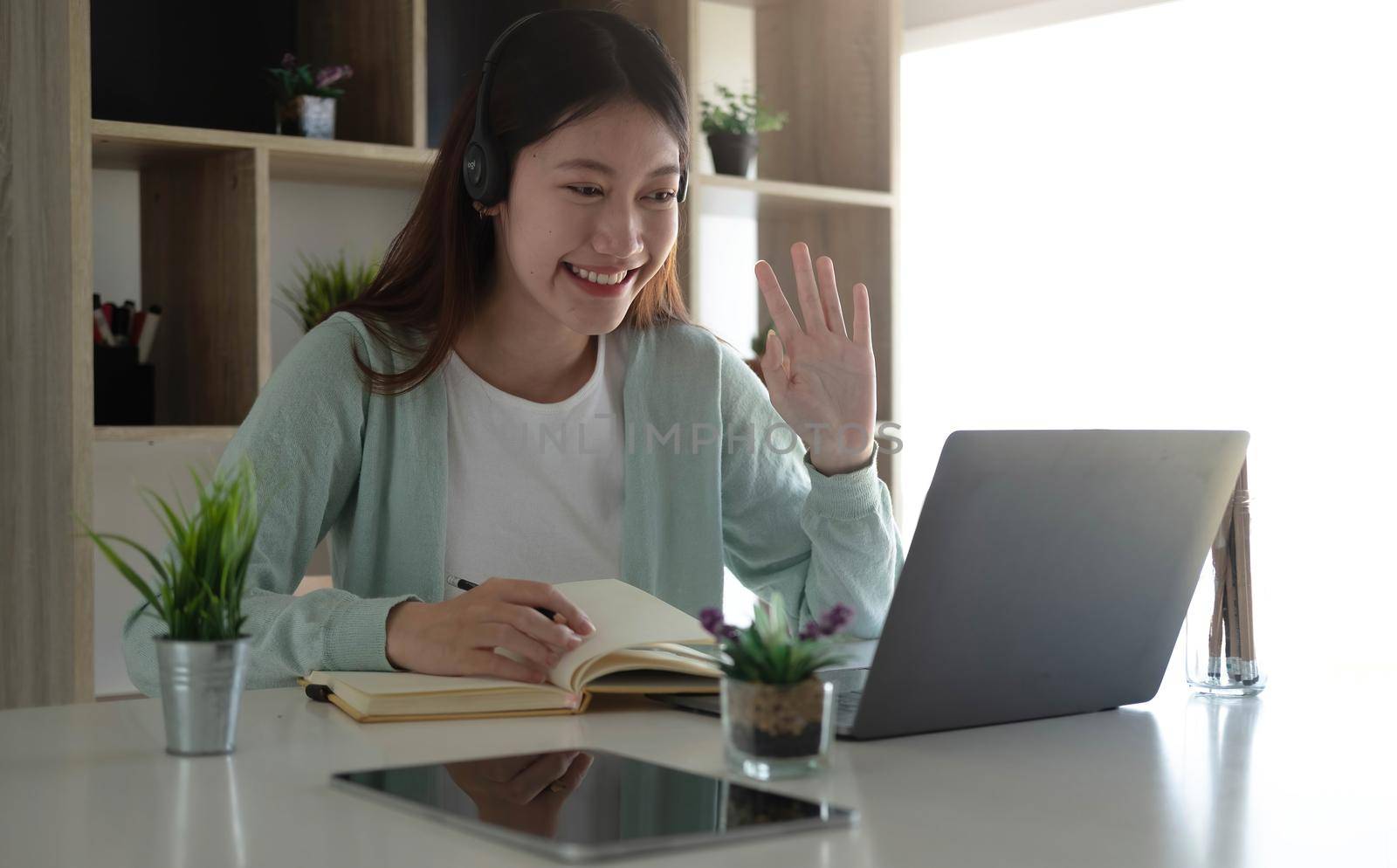 An Asian student in casual clothes is greeting her friend at a video conference. During the time of studying online at home.