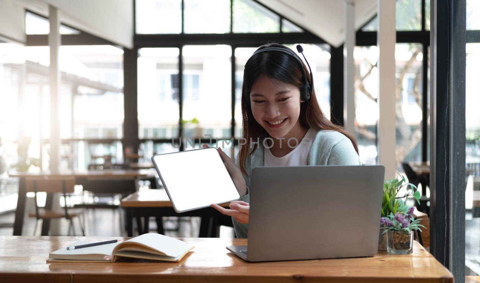 Happy young woman in headphones speaking looking at laptop making notes, girl student talking by video conference call, female teacher trainer tutoring by webcam, online training, e-coaching concept by wichayada