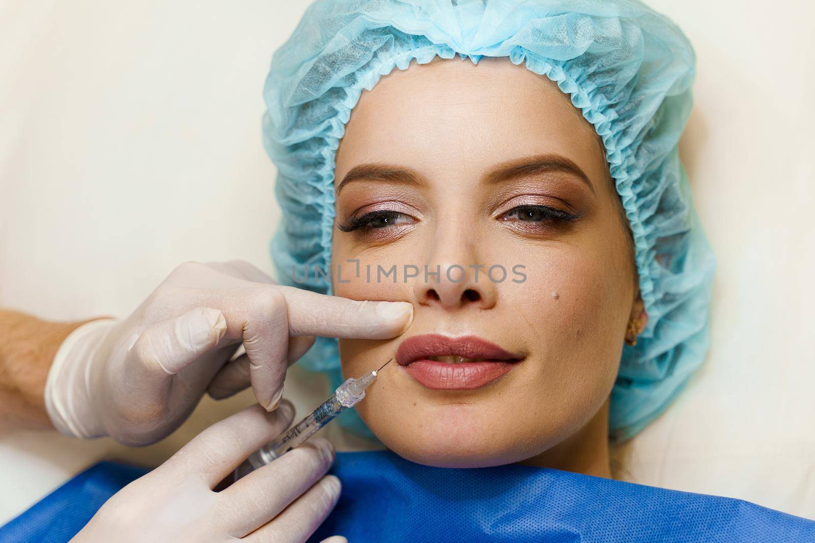 Close-up lips augmentation injections for attractive girl. Plastic surgeon does injection in lips in medical clinic.