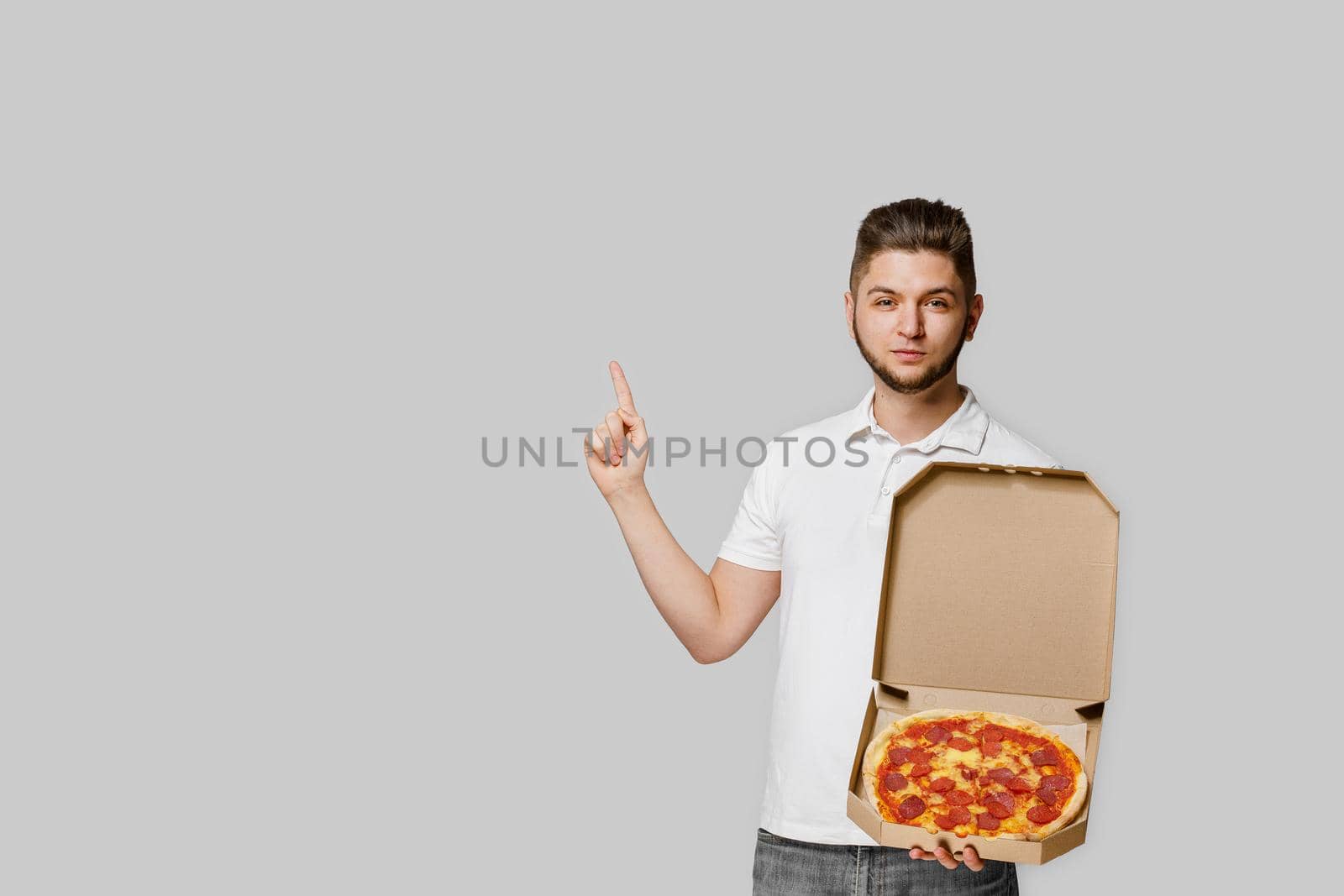 Online pizza safety delivery servise from restaurant. Young caucasian bearded courier points to advertise. Pizza with cheese boards.