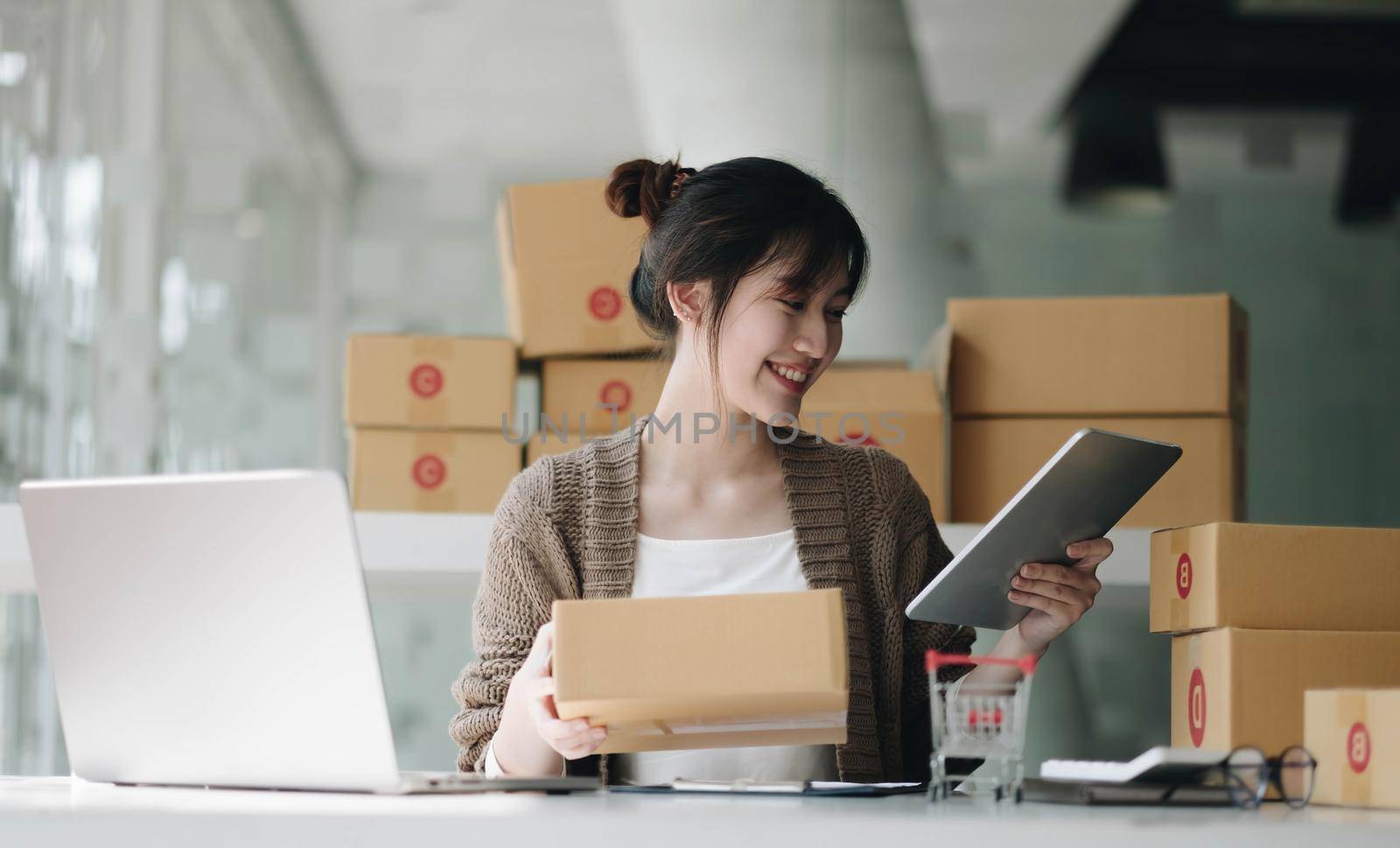 Startup small business entrepreneur SME, asian woman packing cloth in box. Portrait young Asian small business owner home office, online sell marketing delivery, SME e-commerce telemarketing concept by wichayada