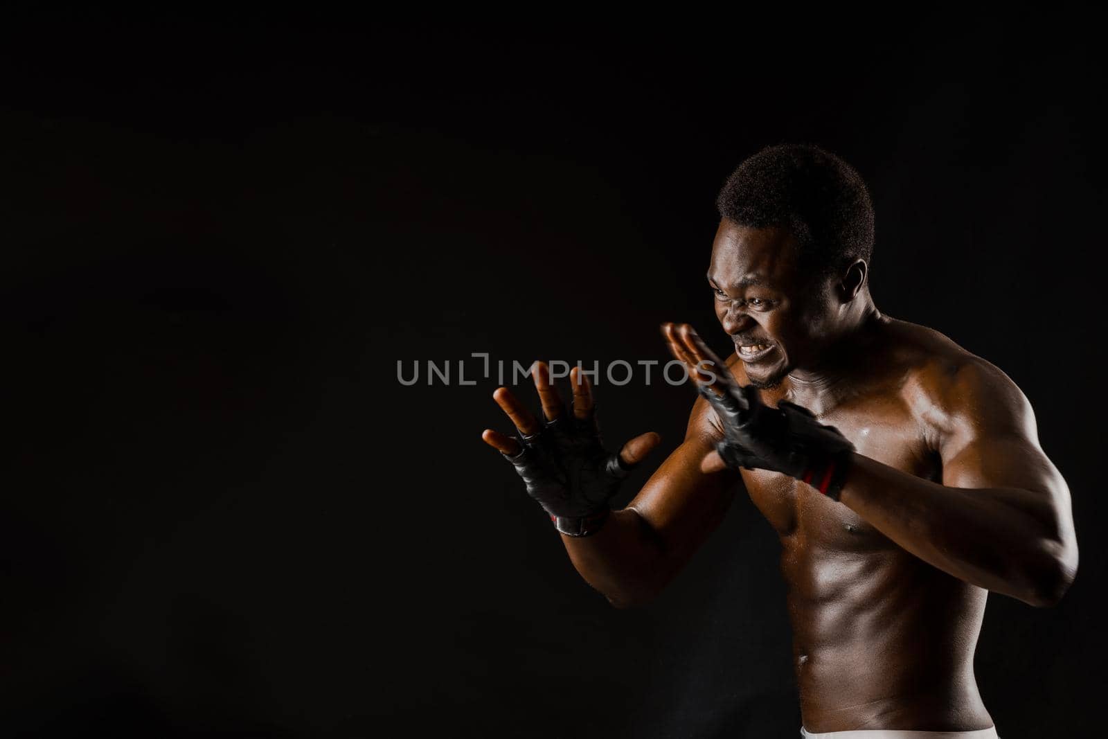Athletic african fighter on black background. Dark skinned undressed man shows a fight. Advert for sport club and gym. Professional boxing and karate. by Rabizo