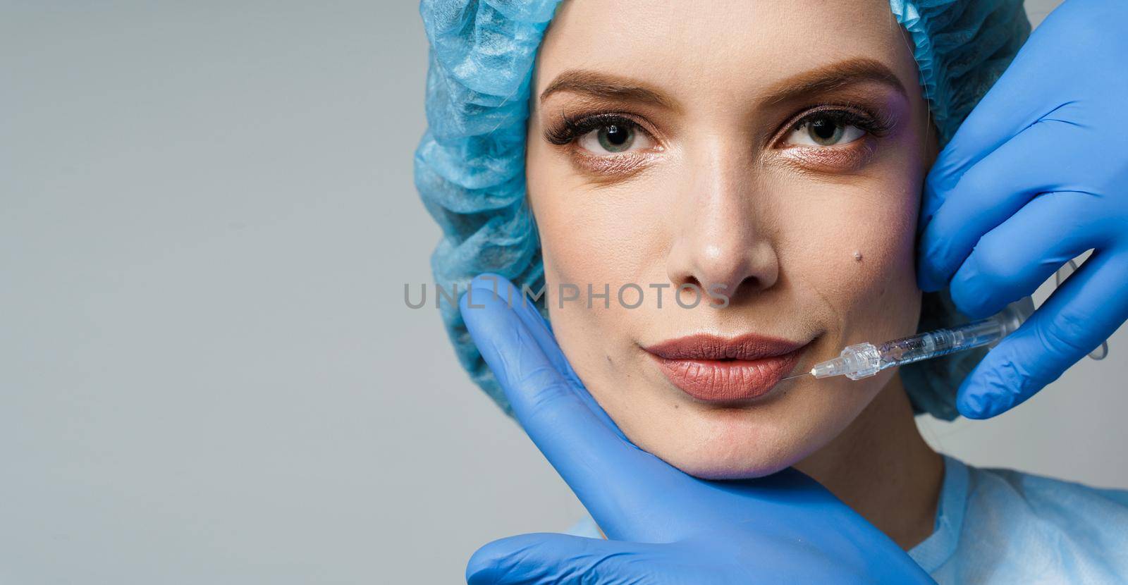 Close-up lips augmentation injections for attractive girl on white background. Plastic surgeon does injection in lip in medical clinic.