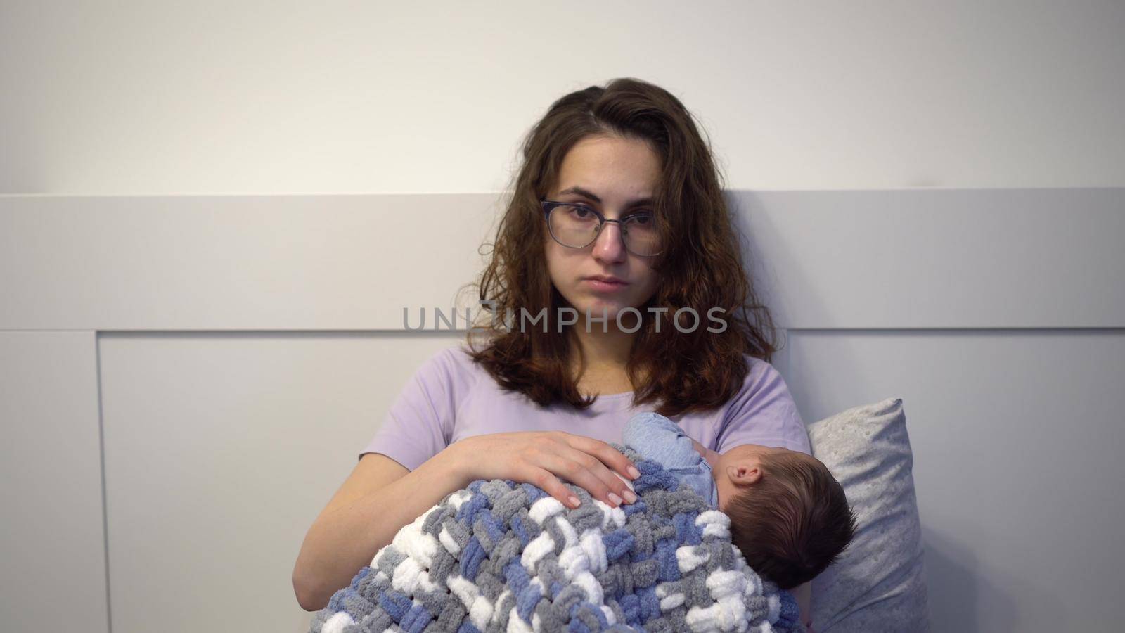 An exhausted young mother cradles a child in her arms in bed. A woman with a frenzied tired look with a newborn in her arms. 4k