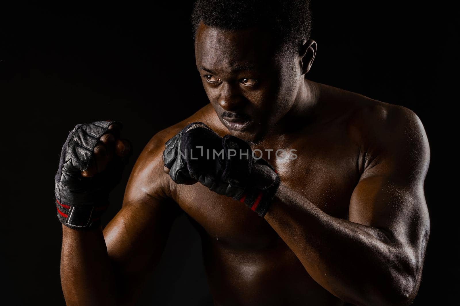 Athletic african fighter on black background. Dark skinned undressed man shows a fight. Advert for sport club and gym. Professional boxing and karate