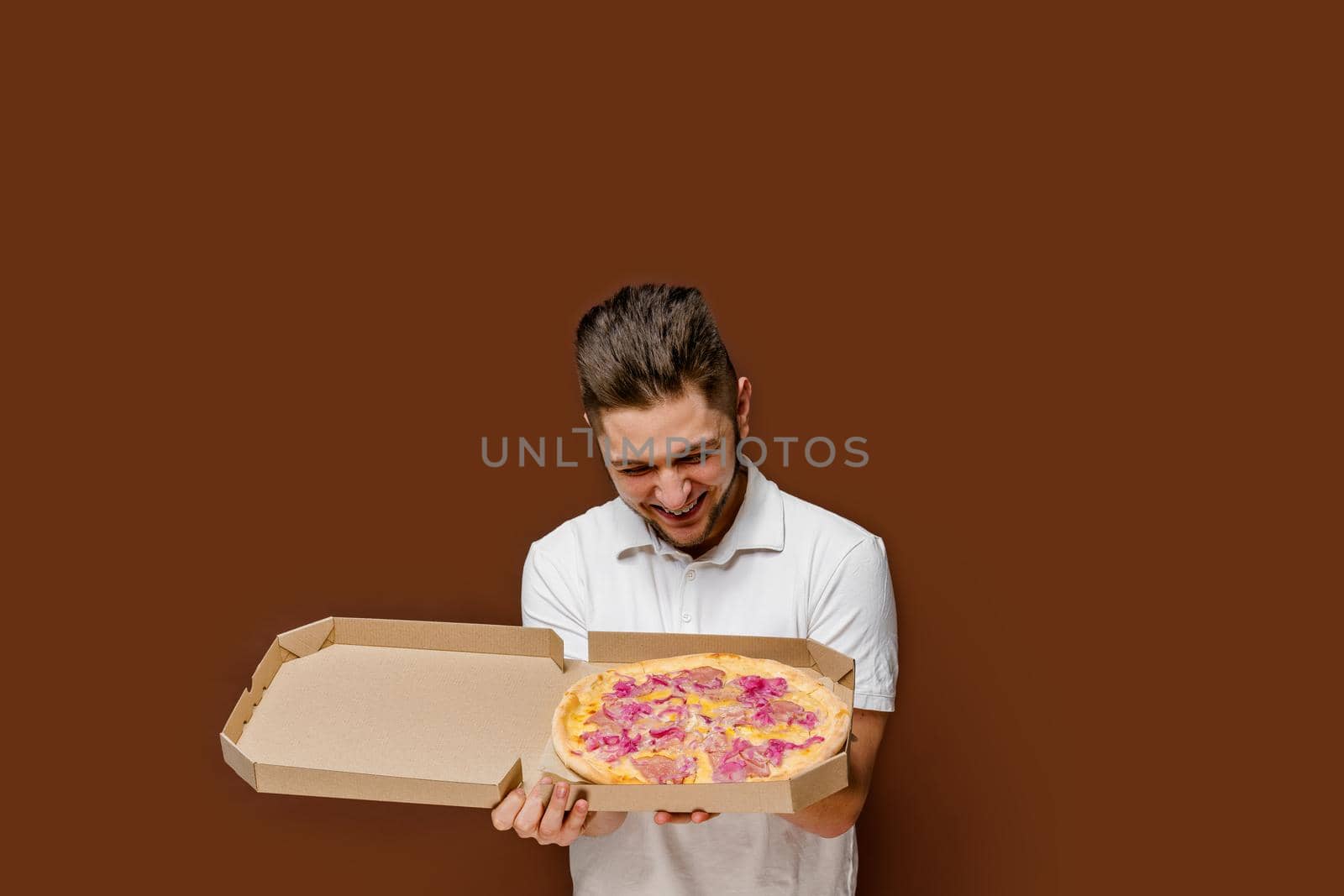 Online pizza safety delivery servise from restaurant. Young surprised courier man sniffs pizza laugh. empty space for advertise.