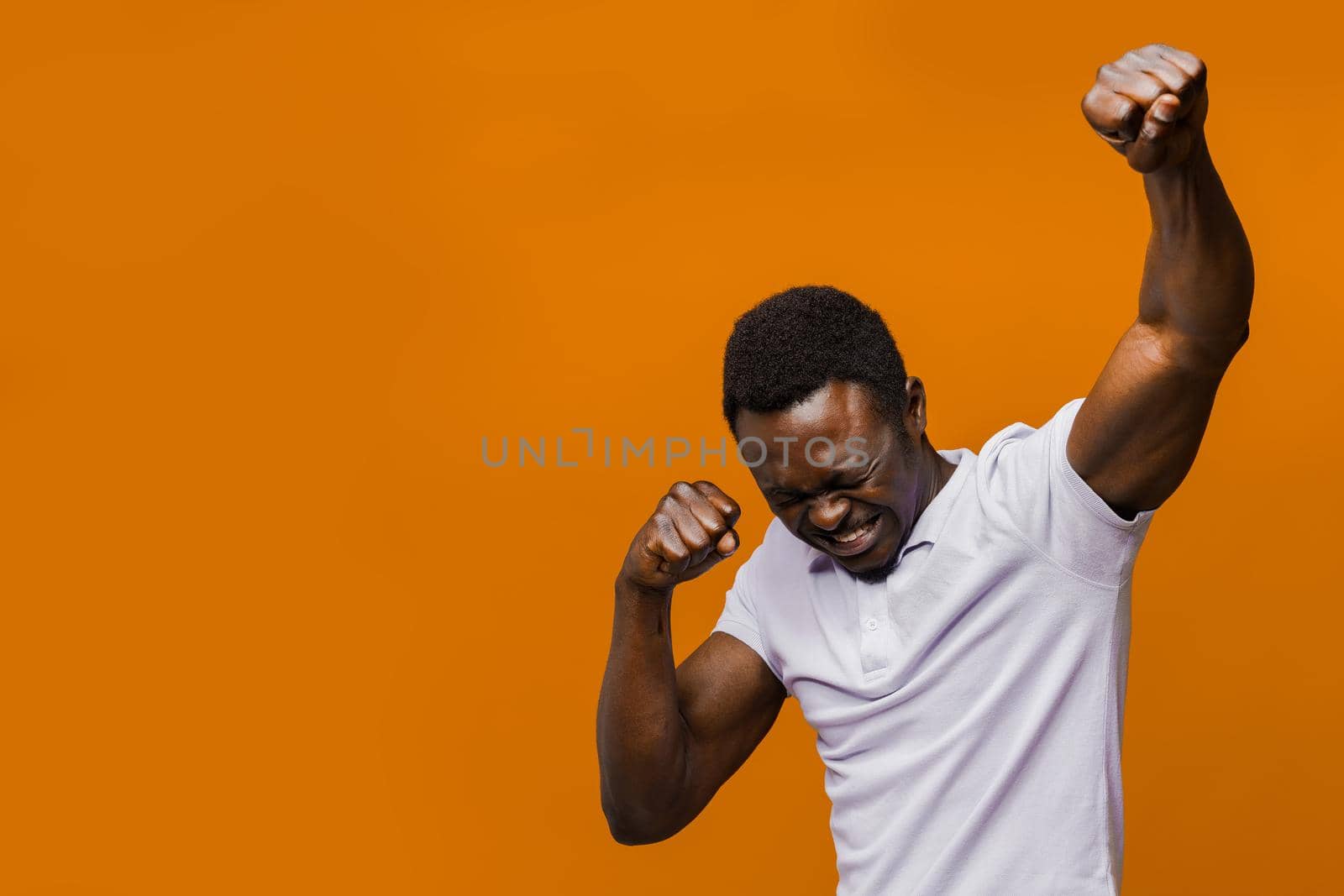 Happy handsome black man in white shirt on orange background with empty place left side. Winning the game by Rabizo