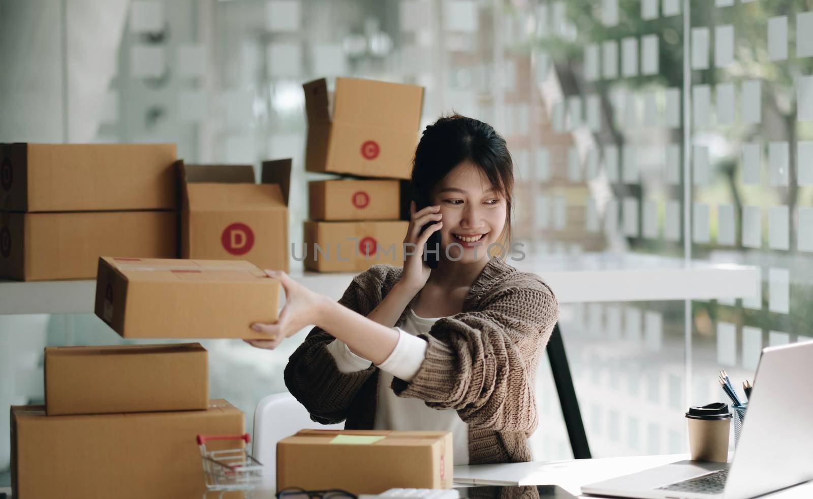 Happy young Asian woman entrepreneur, Smile for sales success after checking order from online shopping store in a smartphone at home office, Concept of merchant business online and eCommerce.