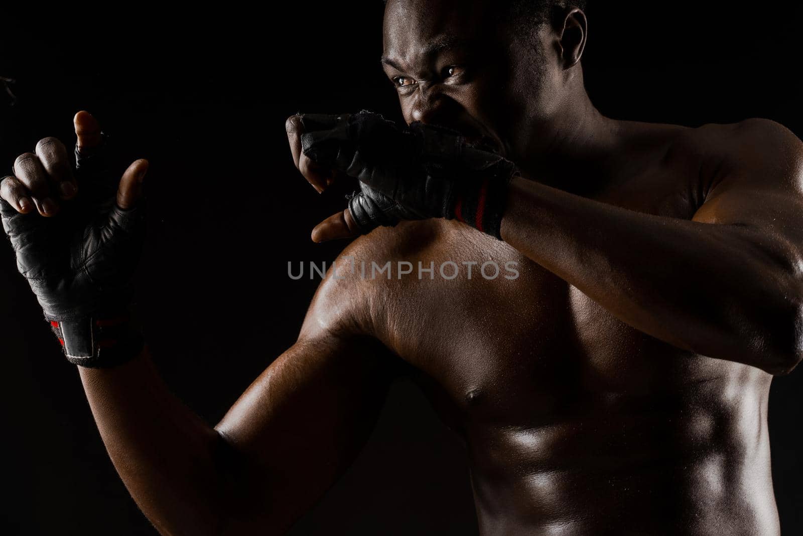 Athletic african fighter on black background. Dark skinned undressed man shows a fight. Advert for sport club and gym. Professional boxing and karate