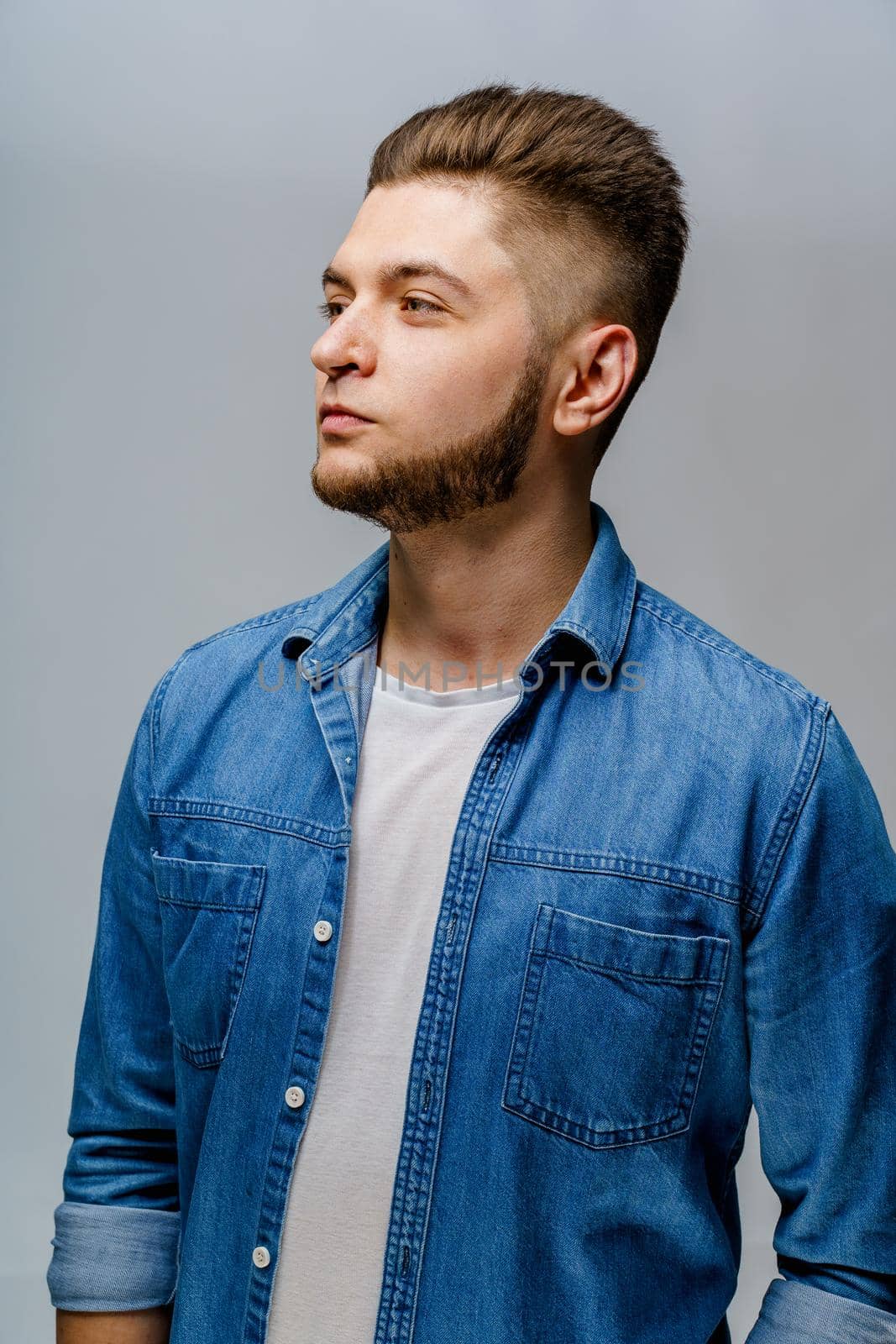 Young handsome man stands over white background and smiles. Confident man wears casual jeans shirt and looks in camera. Bearded business man.