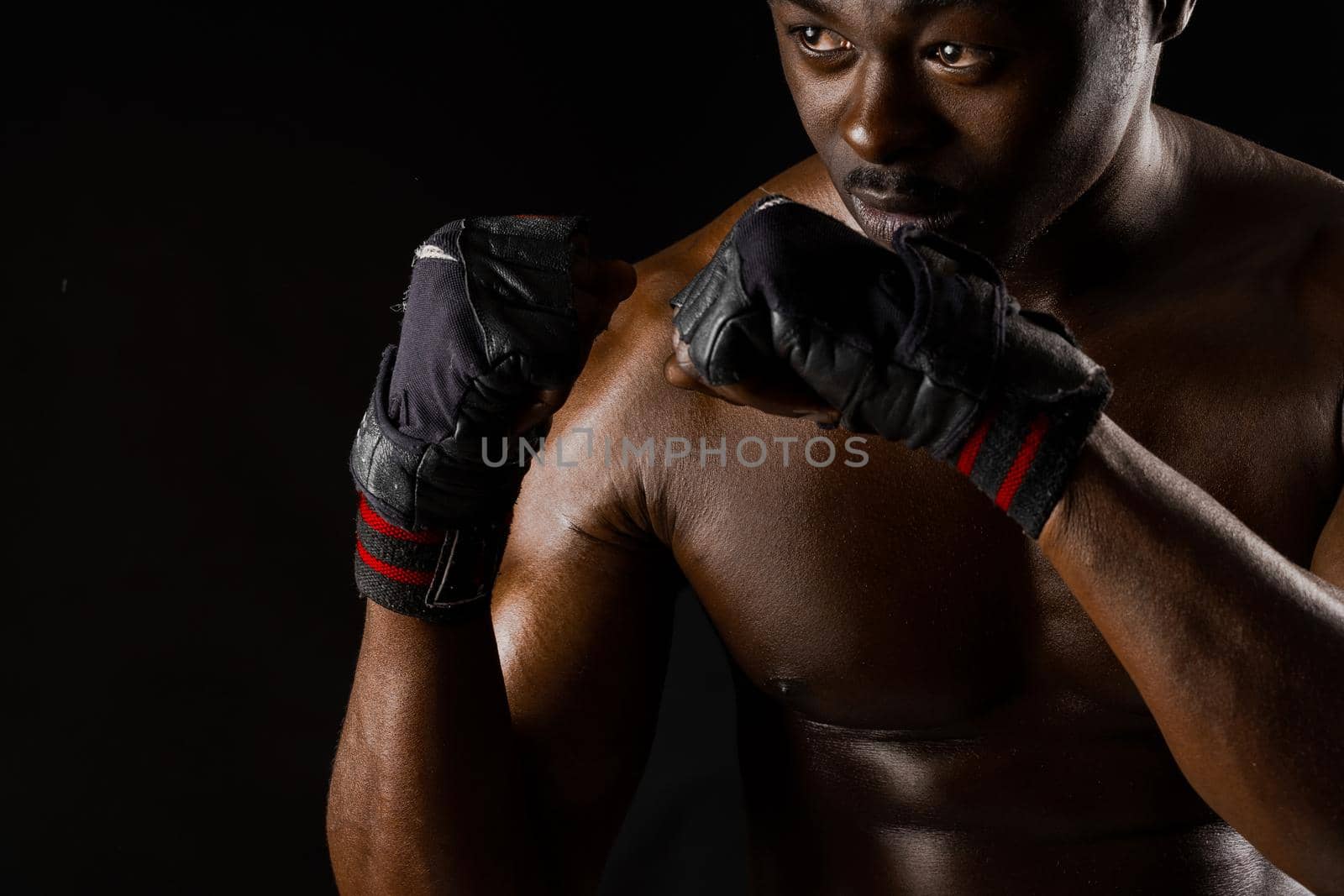 Athletic african fighter on black background. Dark skinned undressed man shows a fight. Advert for sport club and gym. Professional boxing and karate