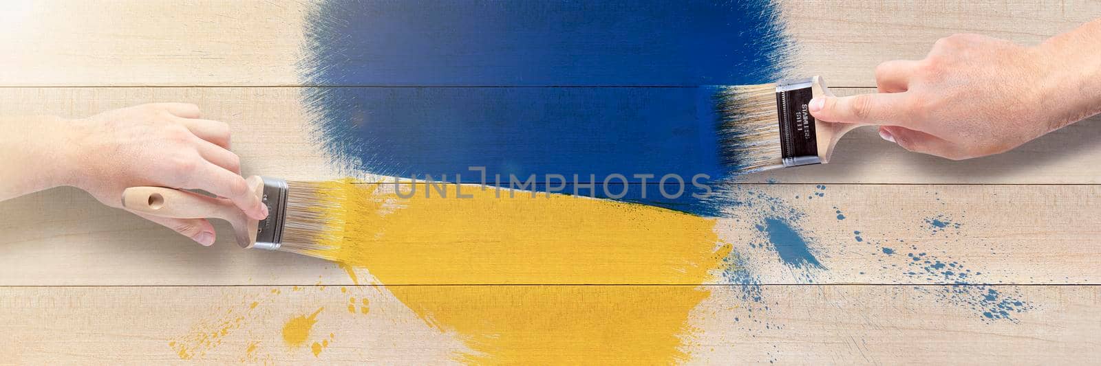 Men's hands with brushes draw a heart in the shades of the Ukrainian flag. Heart in blue and yellow on a wooden background. by SERSOL