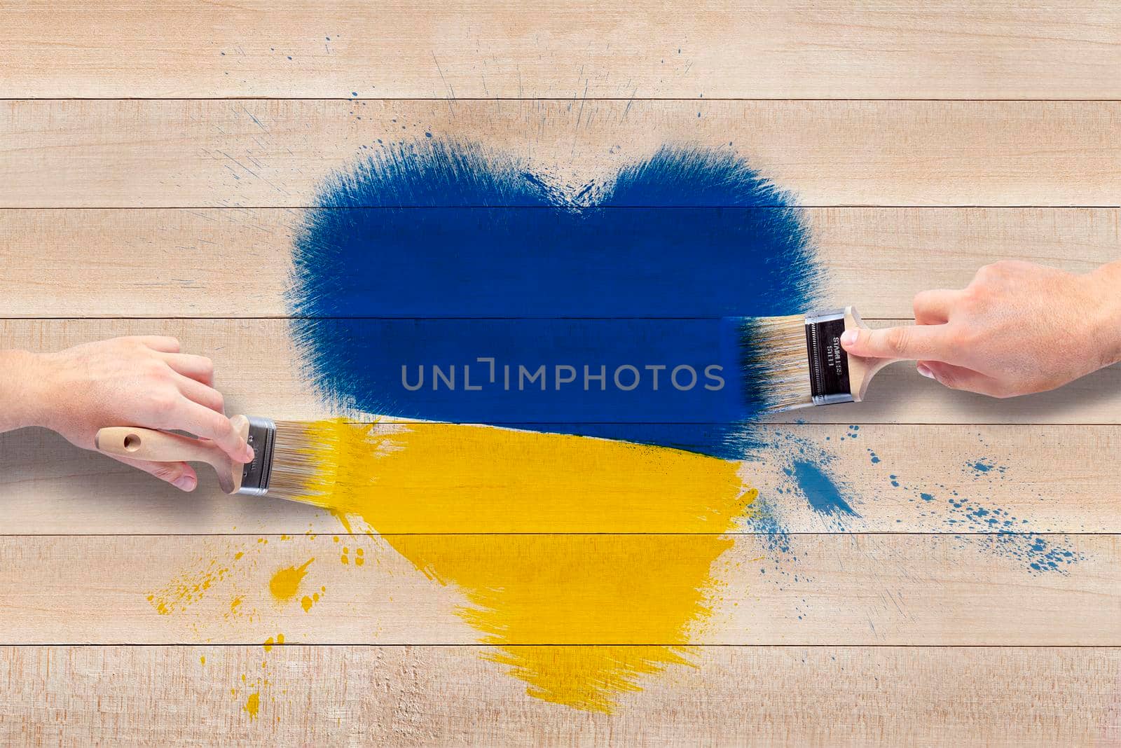 Men's hands with brushes draw a heart in the shades of the Ukrainian flag. Heart in blue and yellow on a wooden background. by SERSOL