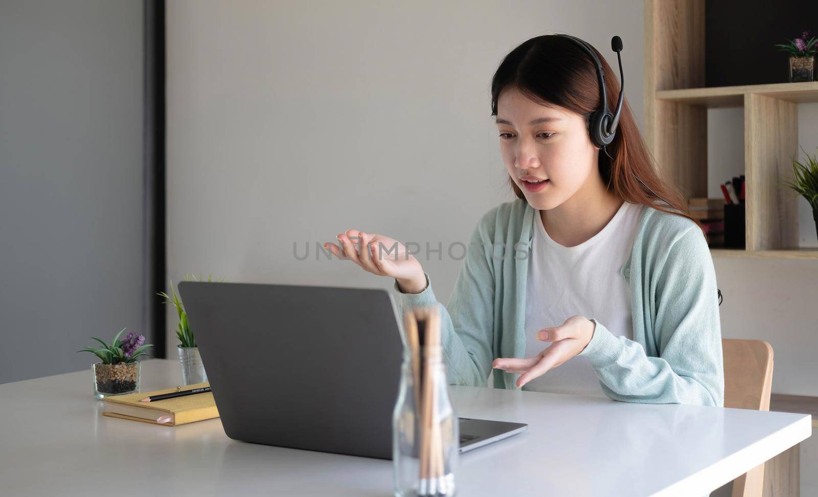 Asian student in casual clothes explaining homework on video conference with teachers on laptop computers at home by wichayada