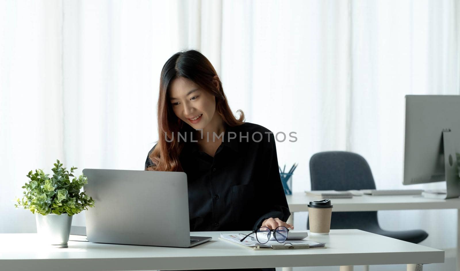 Charming asian businesswoman sitting working on laptop in office. by wichayada