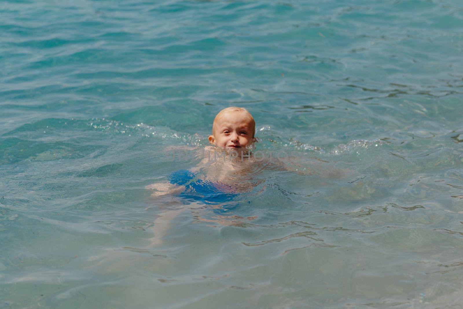 Child learning to swim in the open sea of tropical resort. Kids learn swimming. Exercise and training for young children. Little boy with colorful float board in sport club. Swimming baby or toddler. Happy child boy swims in sea in swimming circle with splash. Blue sky and water. Swimming training. Fun joy activities on vacation in the beach. Childhood moments lifestyle. Freedom careless. boy swim in the sea by Andrii_Ko