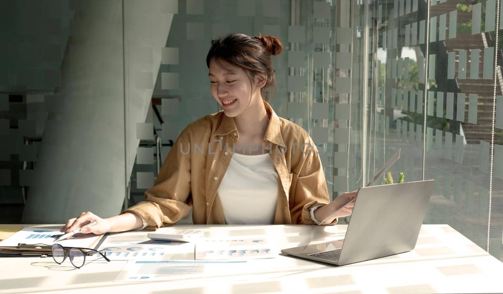 Young Asian businesswoman is happy to work at the modern office using laptop and calculator, working on project, checking financial documents.