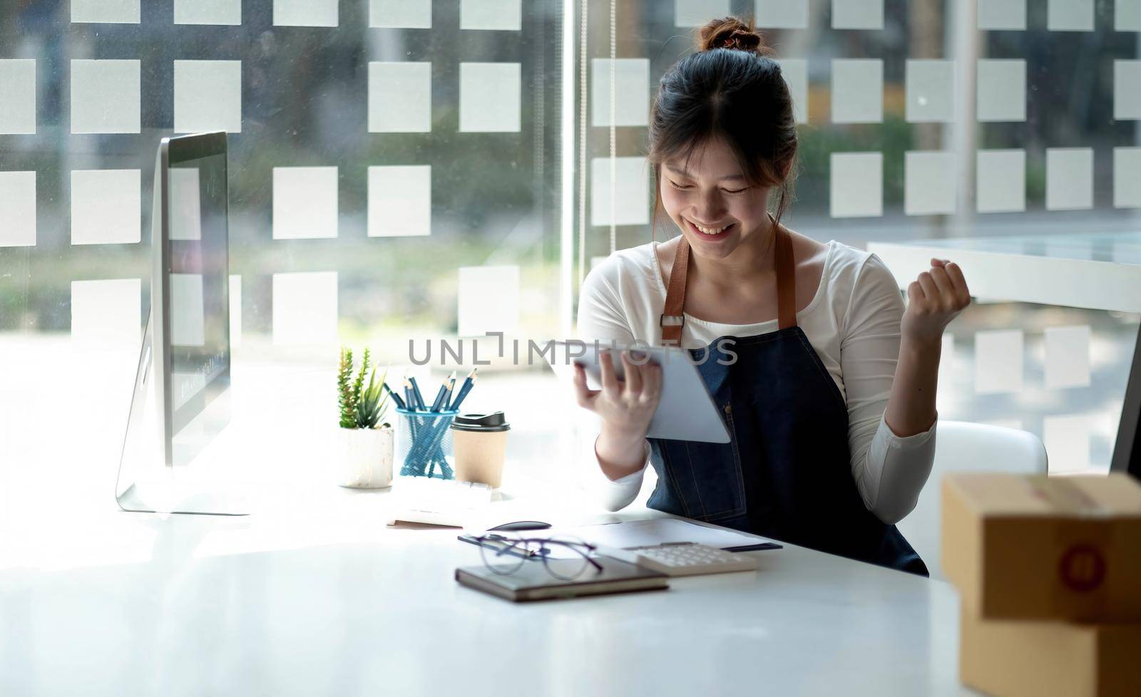 Small business owner wearing an apron is successful selling online using a smartphone parcel box placed at home. by wichayada