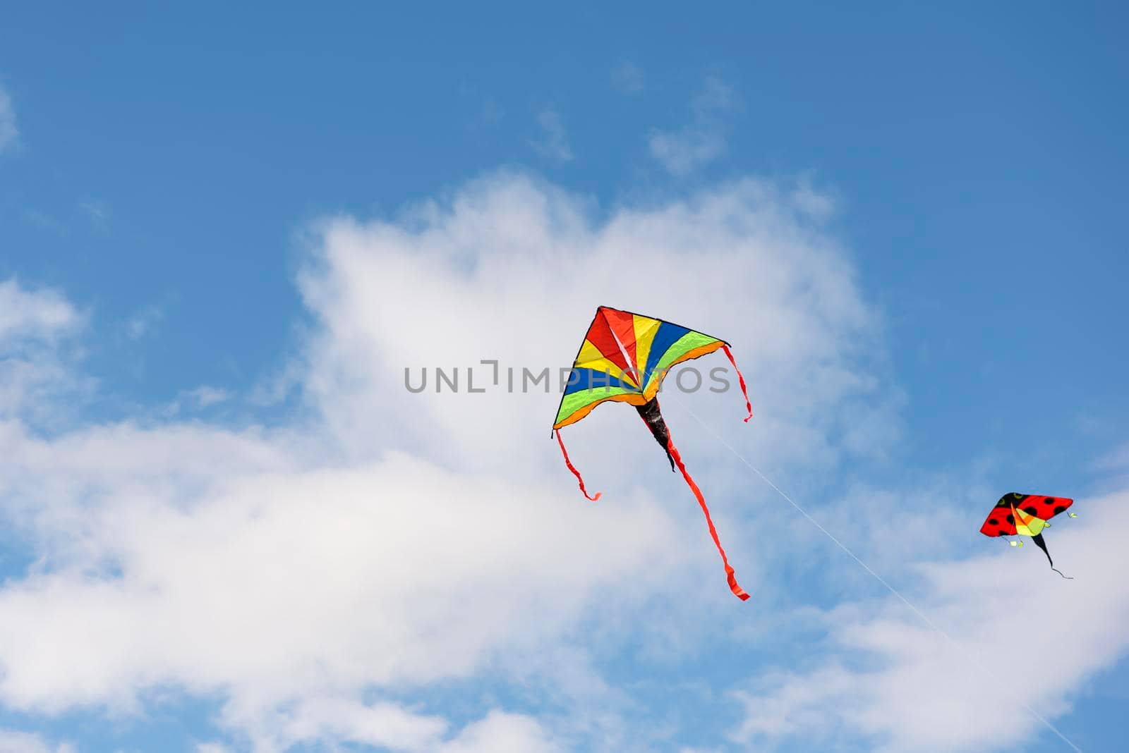 Flying kite. A multi-colored kite is flying in the sky. Blue sky with clouds and sun. Space for text or copy space. by SERSOL