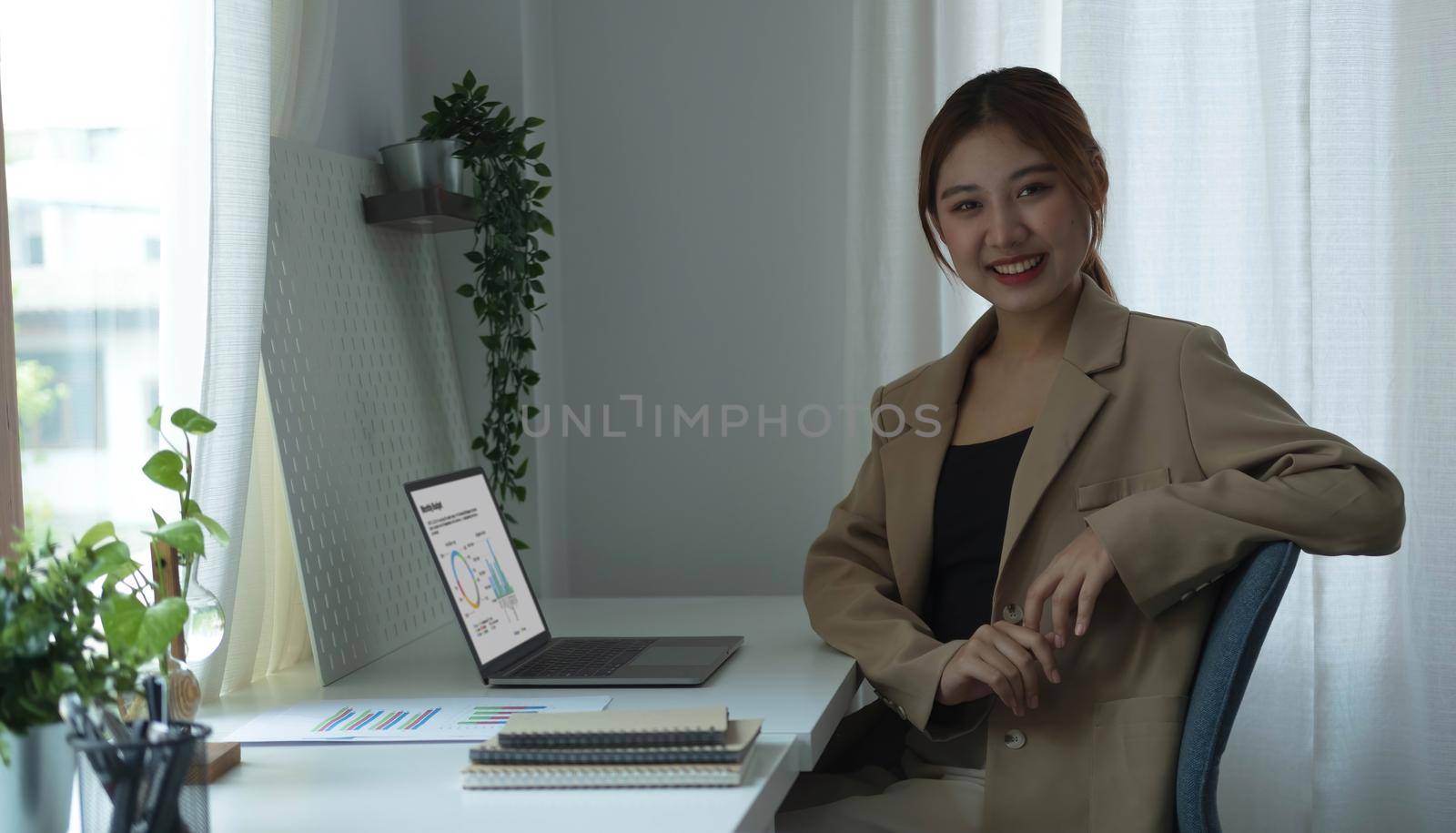 Portrait of confident young entrepreneur sitting at modern workplace and smiling to camera..