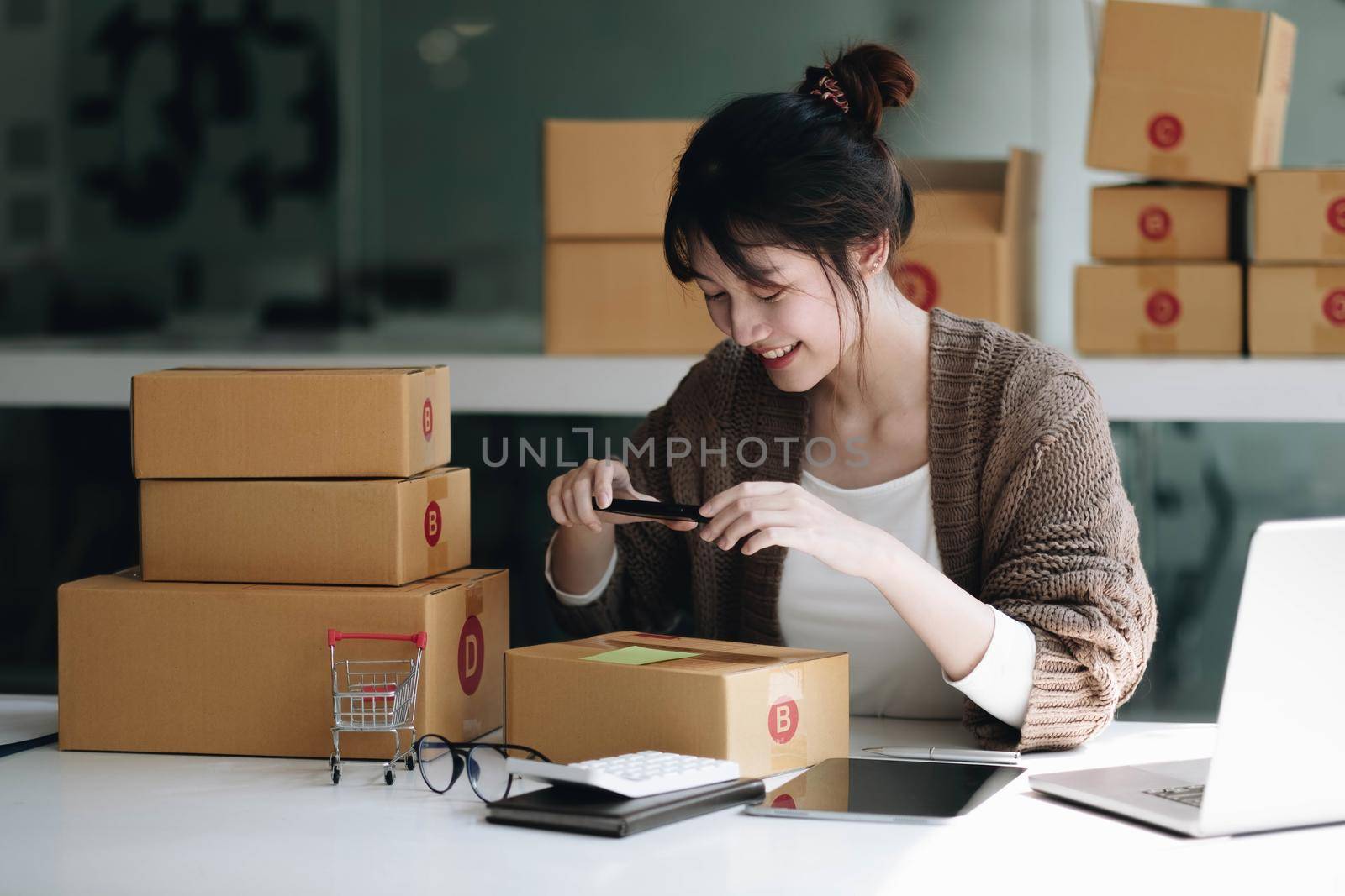 Startup small business SME, Entrepreneur owner using smartphone or tablet taking receive and checking online purchase shopping order to preparing pack product box. Selling online ideas concept.