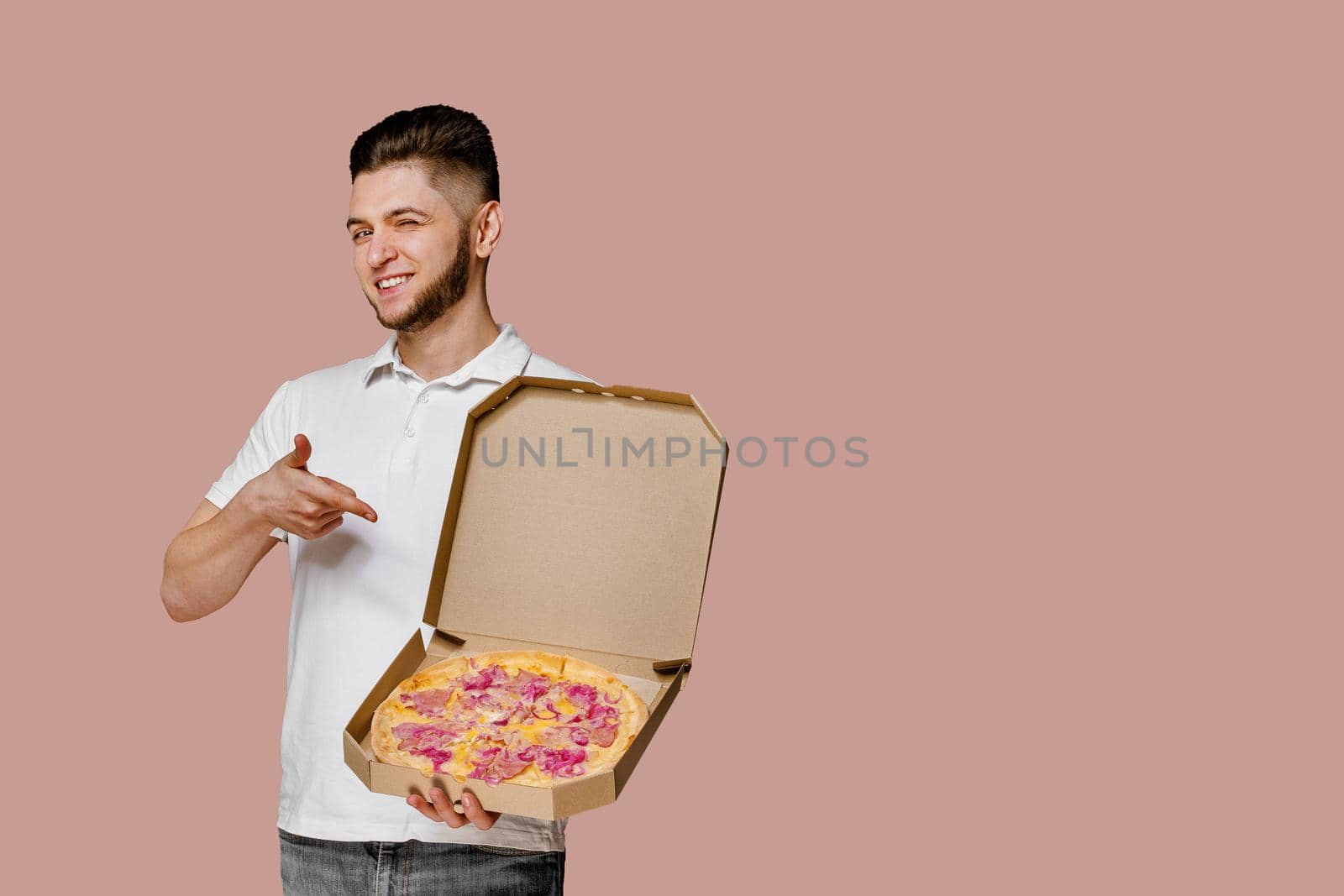 Handsome yound courier with points to pizza. Empty space for text advertise. Safery delivery from restaurant. Confident student works courier. by Rabizo