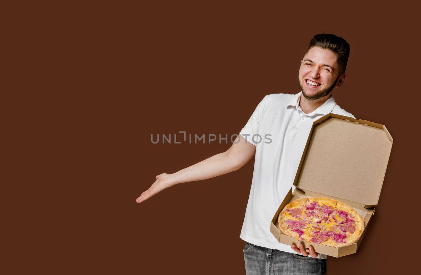 Online pizza safety delivery servise from restaurant. Young surprised courier man smiles and points to empty space for advertise