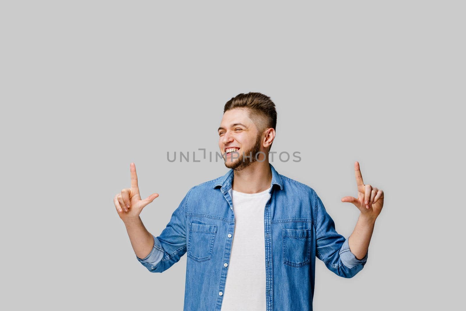 Pointing up. Emotional young handsome man points his fingers up for choose. Empty space for advertise. Caucasian man stants over white background