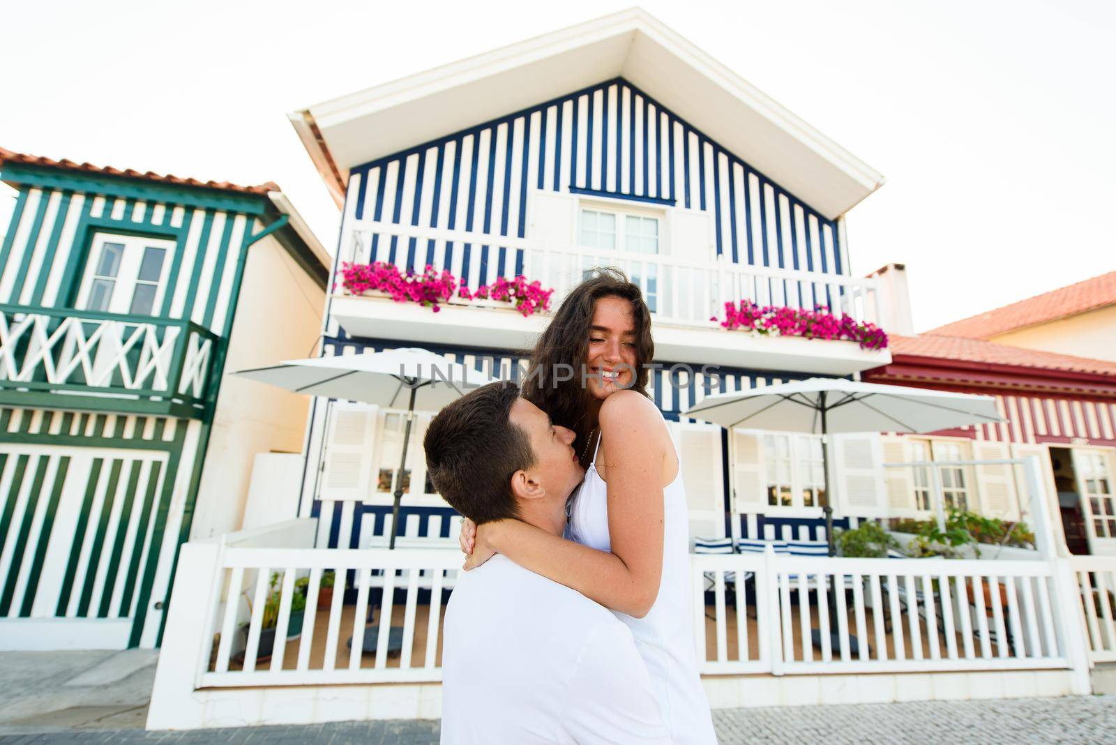 Handsome man puts up his girlfriend and kisses in Aveiro, Portugal near colourful and peaceful houses. Lifestyle of couple in love.