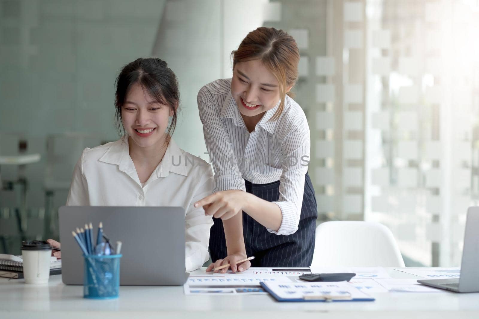 Two young Asian businesswoman discuss investment project working and planning strategy. Business people talking together with laptop computer at office..